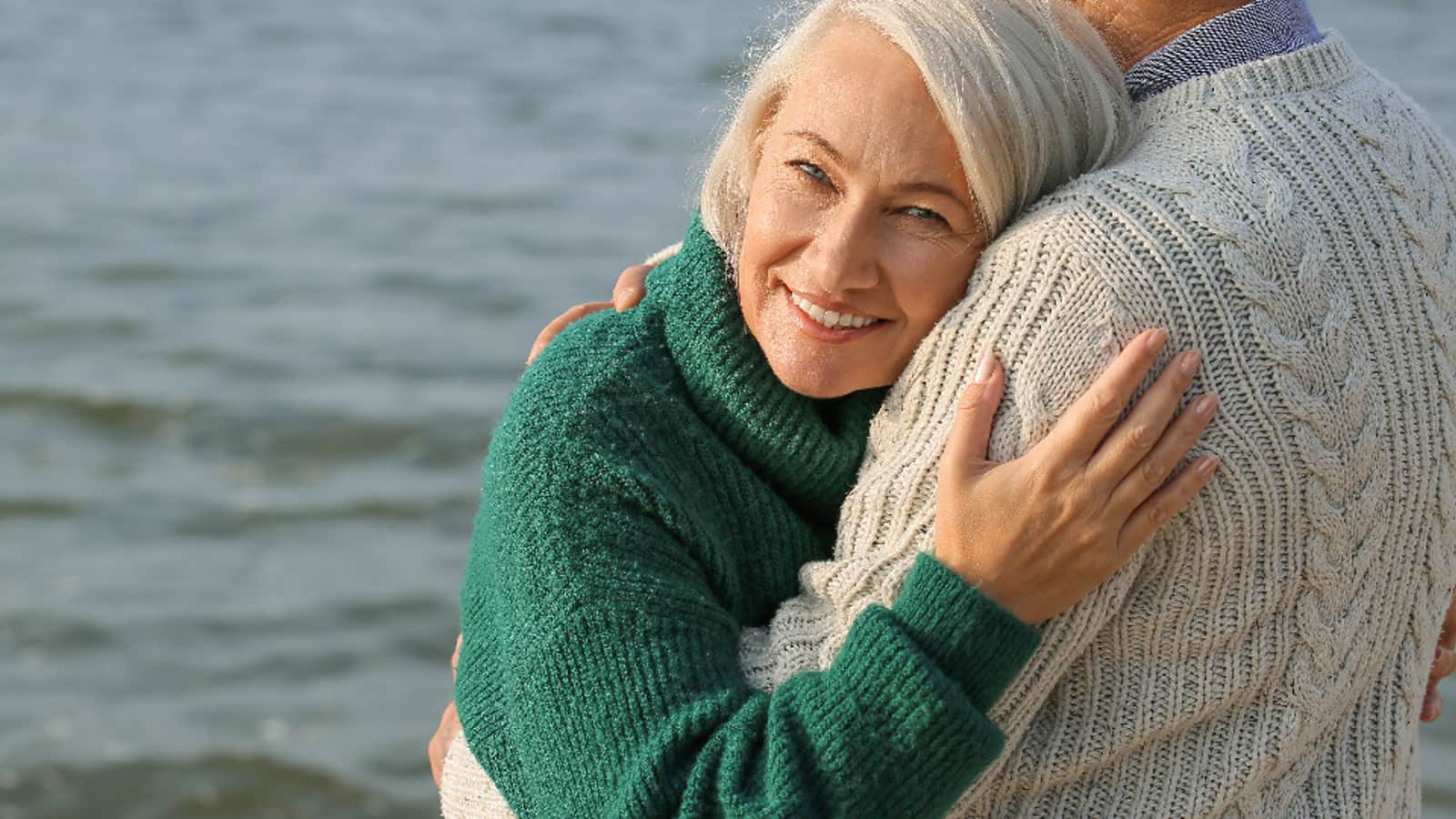 An older couple standing together outdoors by the water
