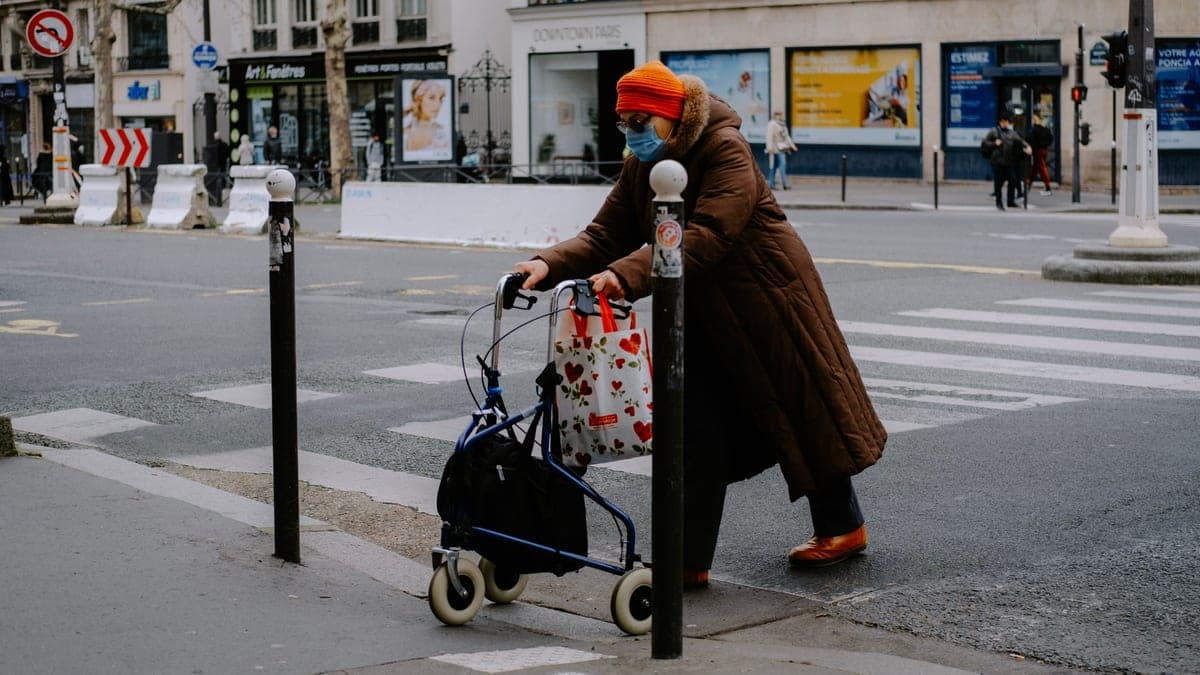 An older woman crossing a street with a four-wheeled rollator